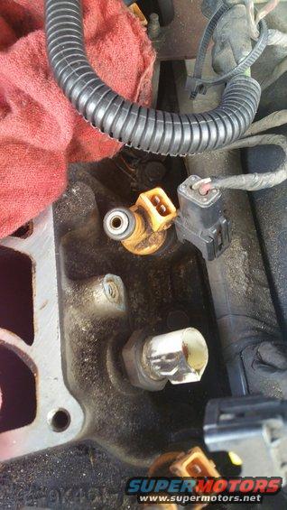 Close-up of a yellow fuel injector and electrical connector on an engine block, with a red rag and black tubing visible