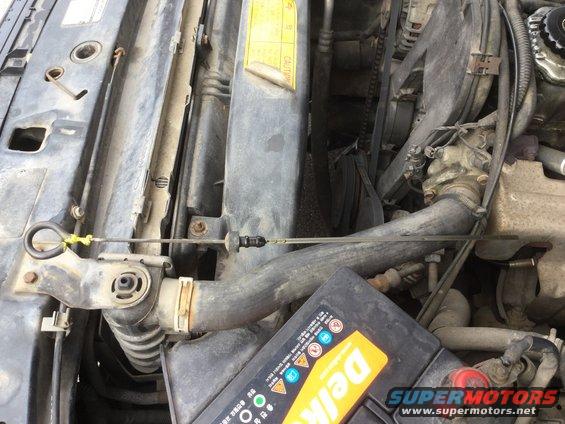 Engine bay with radiator, battery, and belts visible. Yellow caution sticker on radiator
