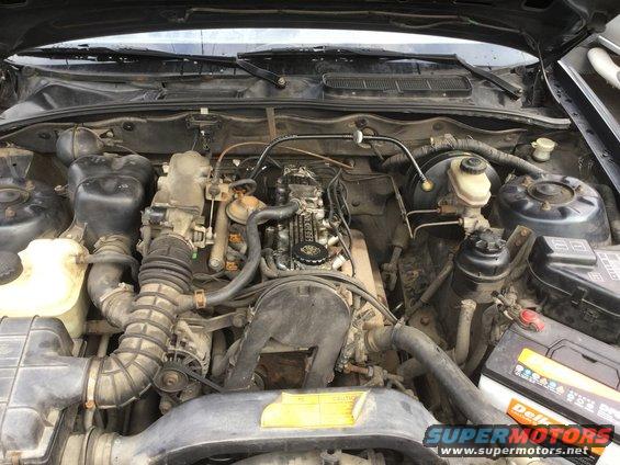 1995 Holden Astra engine bay, showing engine, battery, and various hoses. The engine appears to be a 4-cylinder