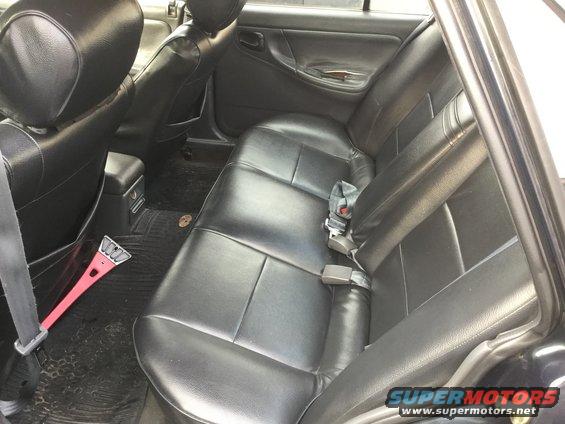 Back seat of a car with black leather seats. Ice scraper on the floor