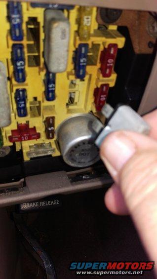 Hand holding a relay near a vehicle fuse box with multiple fuses and relays installed