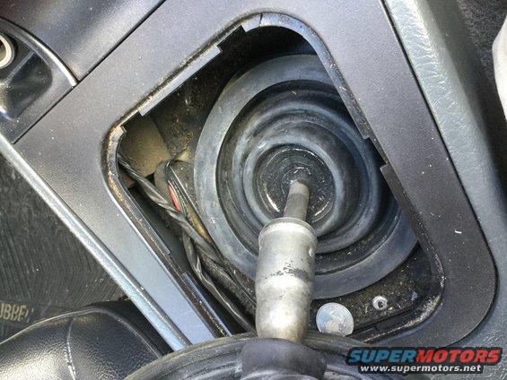 Close-up of a car's gear shifter boot and surrounding console area. Wires are visible underneath the boot