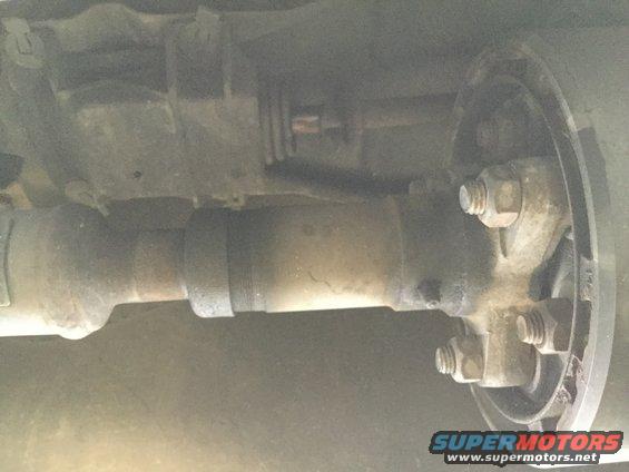 Close-up of a vehicle's driveshaft connected to a brake drum assembly with visible bolts and nuts