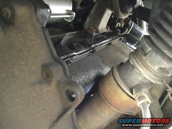 Close-up of engine oil pan with visible oil residue and part of exhaust pipe