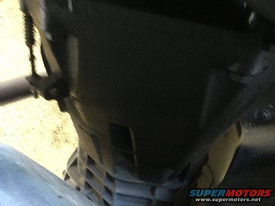 Black engine component with visible texture and a metal pipe. Supermotors.net logo in lower right