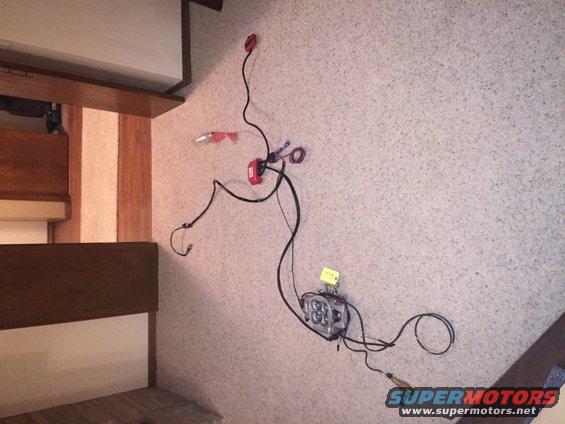 Wiring harness with red connectors and a square LED light assembly attached to a textured wall