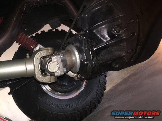 Drivetrain components including driveshaft, U-joint, and differential housing. Tire visible
