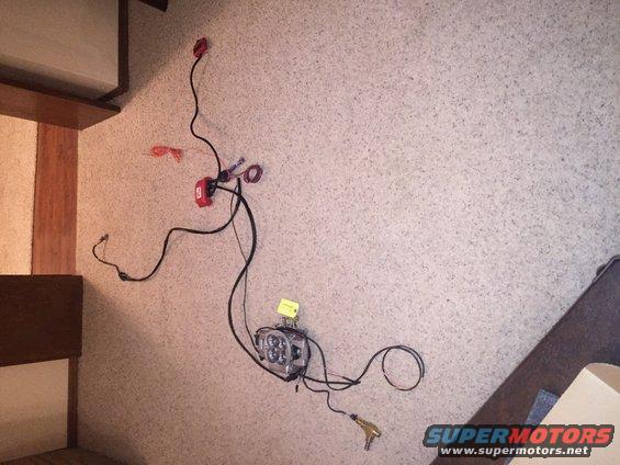 Wiring harness with red relay box and a clear-lensed LED light bar, laid out on a carpeted surface