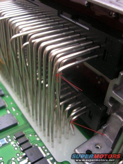 Close-up of circuit board with metal pins and red arrows pointing to bent pins