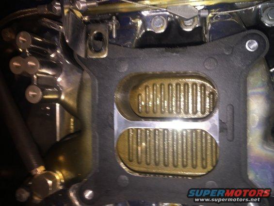 Close-up of a carburetor intake manifold gasket with visible fuel lines and linkage