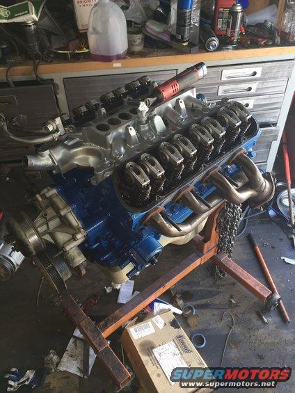 Engine on an orange engine stand, blue painted block, silver intake manifold, exhaust manifolds attached