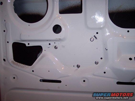 White vehicle door interior with black spray paint overspray and visible screw holes