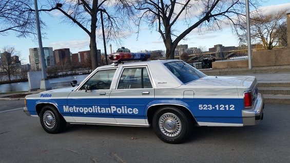 Police car, white and blue, side view, with "Metropolitan Police" text and emergency lights