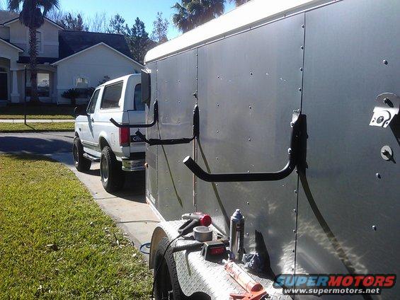 White SUV with ladder rack towing a silver cargo trailer. Tools on trailer fender