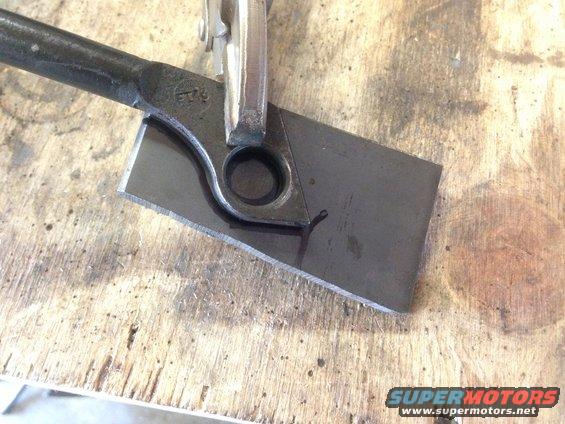 Metal part clamped in vise, being cut with a tool on a wooden workbench