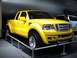 1995 Ford Bronco - A bright yellow Ford F-150 pickup truck is displayed at an auto show, with another vehicle visible in the background.