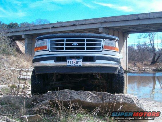 Front view of a lifted Ford F-250 truck parked on rocks near a river, under a bridge