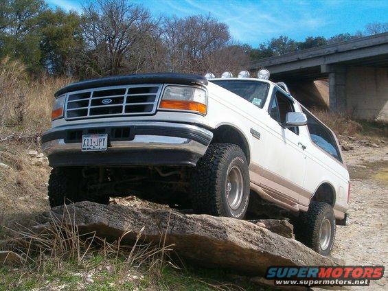 White 1996 Ford Bronco with aftermarket lights on roof, driving over rocks