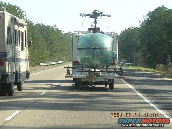 RV on left, trailer with green tank and helicopter rotor on right, driving on highway