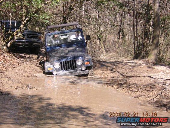 Dark blue Jeep Wrangler stuck in mud puddle, front grille visible