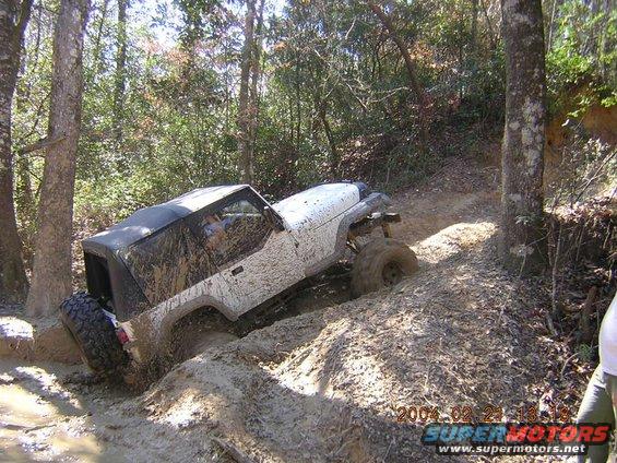 Mud-covered Jeep Wrangler navigating a muddy trail in a wooded area