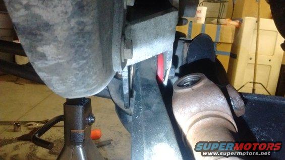 Close-up of vehicle suspension parts, including a driveshaft U-joint and a red bushing, with a jack stand visible