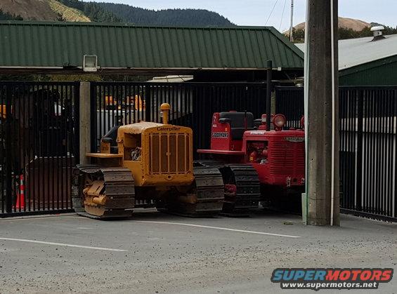 Yellow Caterpillar tractor and red International tractor parked behind a fence