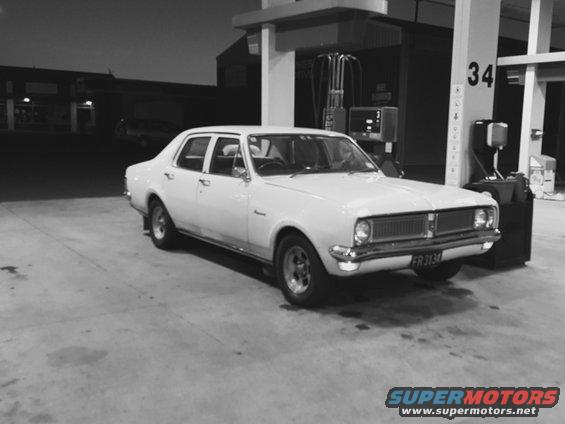 White sedan with a horizontal grille and round headlights parked at a gas station. License plate reads FR 3134