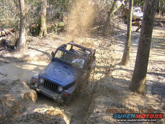 Blue Jeep Wrangler splashing through mud on a trail