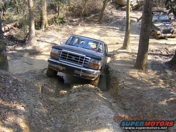 Ford Bronco navigating a muddy rut with a Jeep in the background