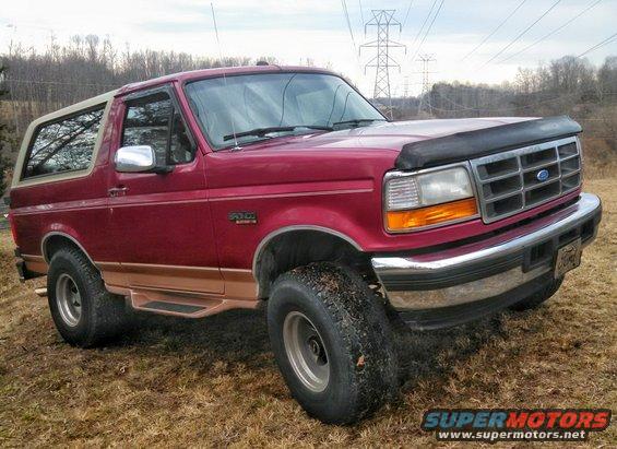 Red Ford Bronco with tan top, lifted on large tires, viewed from the front-right