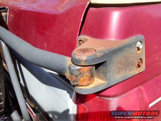 rusted trailer hitch mount attached to the rear corner of a red vehicle