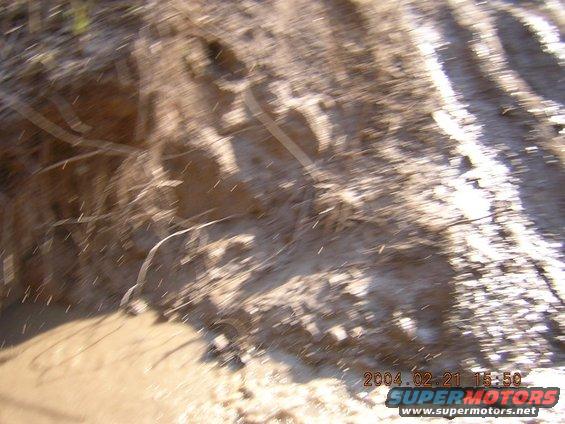 muddy ground with tire tracks and some debris, timestamp 2004.02.21 15:50