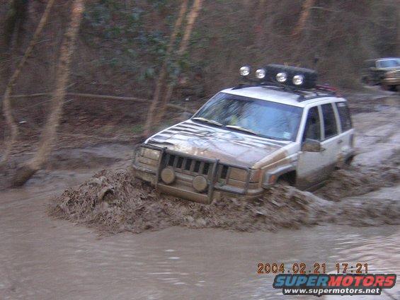 Tan and white Jeep Grand Cherokee stuck in mud, front bull bar, roof rack with lights