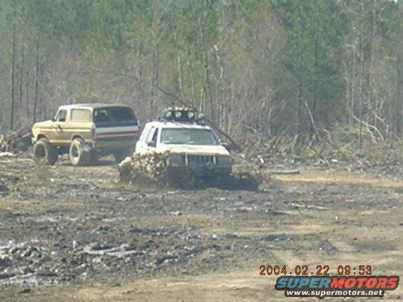 Tan 1980s Ford Bronco and a white Jeep Cherokee stuck in mud
