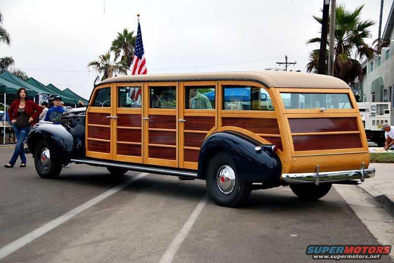 long woodie station wagon with dark blue fenders and roof, American flag on pole