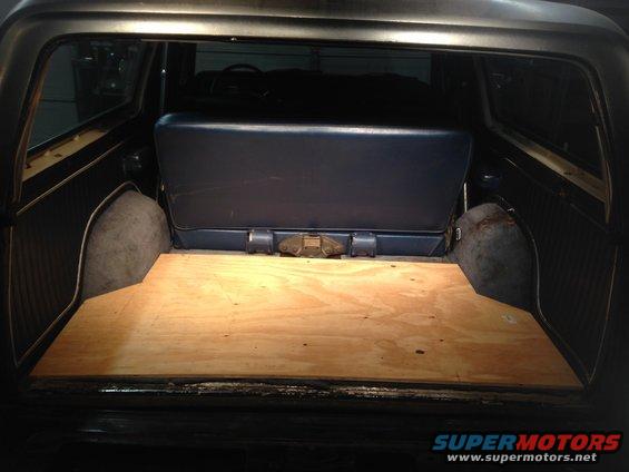 Rear cargo area of a dark SUV with a wooden floor and a blue bench seat. The wheel wells are visible
