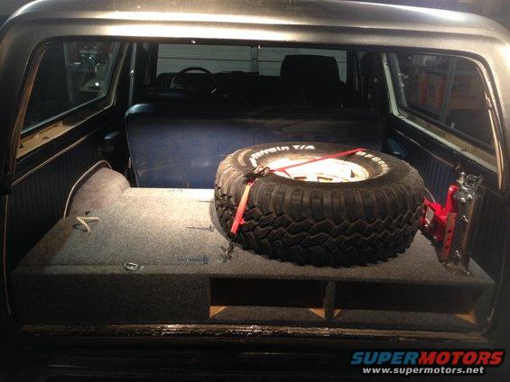 Spare tire and jack secured in a carpeted storage compartment inside a dark-colored vehicle