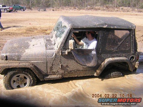 Muddy black Jeep Wrangler stuck in mud, driver visible