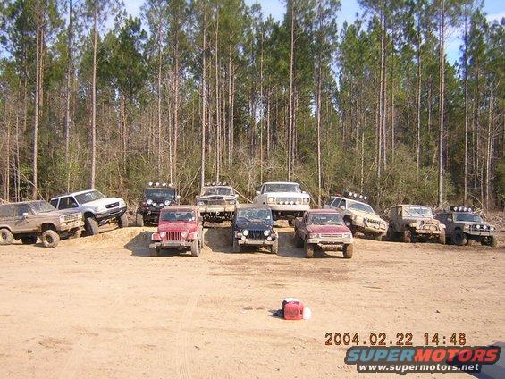 Several off-road vehicles parked on a dirt lot with trees in the background