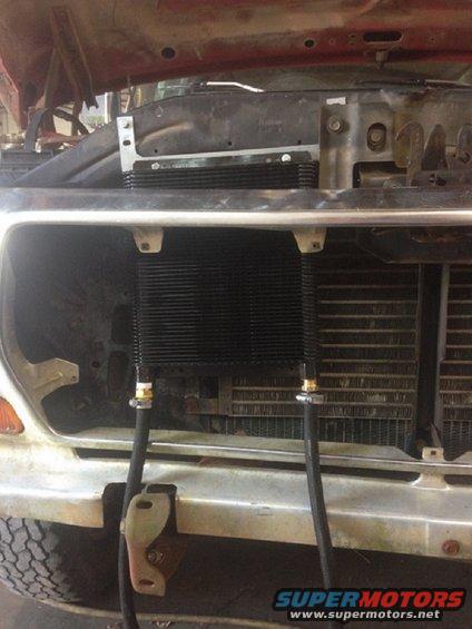 Front end of a vehicle with a new transmission cooler installed in front of the radiator. Hoses run from the cooler