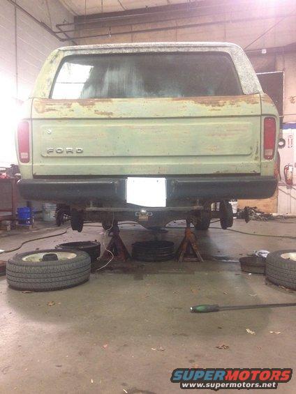 Green 1978 Ford Bronco rear view on jack stands, with rust on the tailgate and rear quarter panels