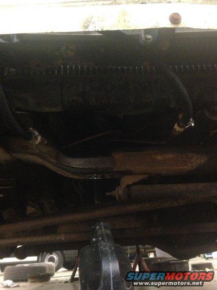 Underside view of vehicle showing suspension components and hoses. A black oil drain pan is visible