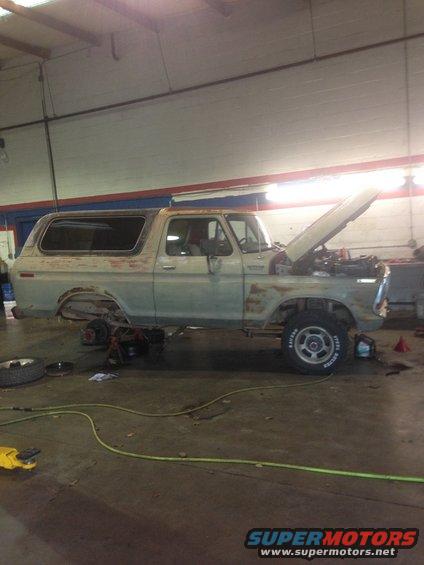 1978 Ford Bronco in a garage, hood up, undergoing repairs, with rust visible