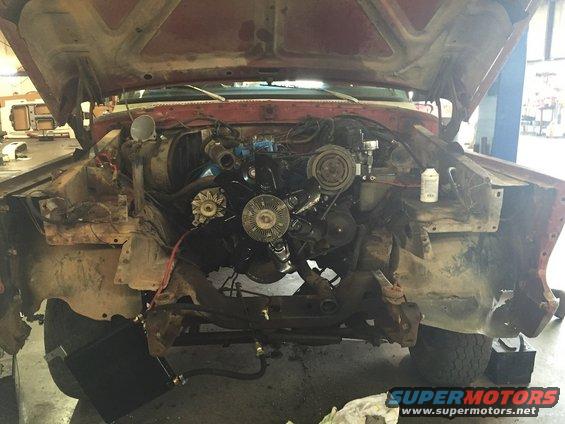 Engine bay of a red vehicle with hood open, showing engine components and front chassis