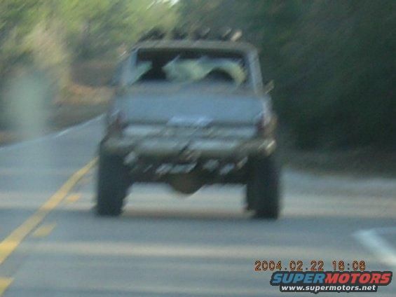 Rear view of lifted SUV with roof rack, driving on a road
