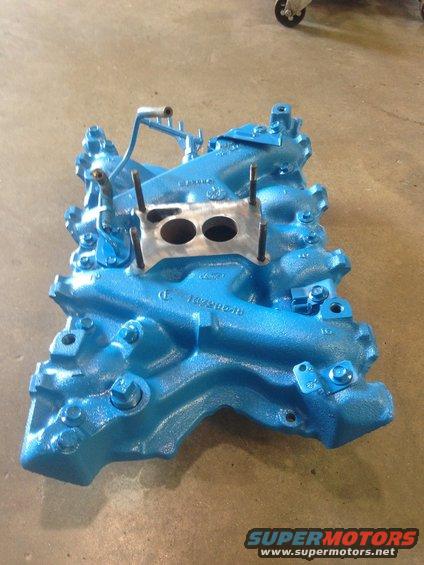 Blue intake manifold with two carburetor openings and metal mounting plate