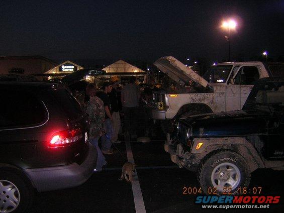 White SUV with hood open, dark SUV in foreground, people gathered