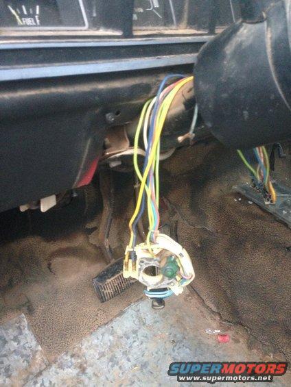 Interior view of a vehicle's steering column with exposed wiring and a fuel gauge visible