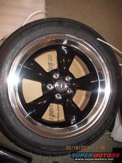 Black five-spoke aftermarket wheel with polished lip and tire, box visible behind